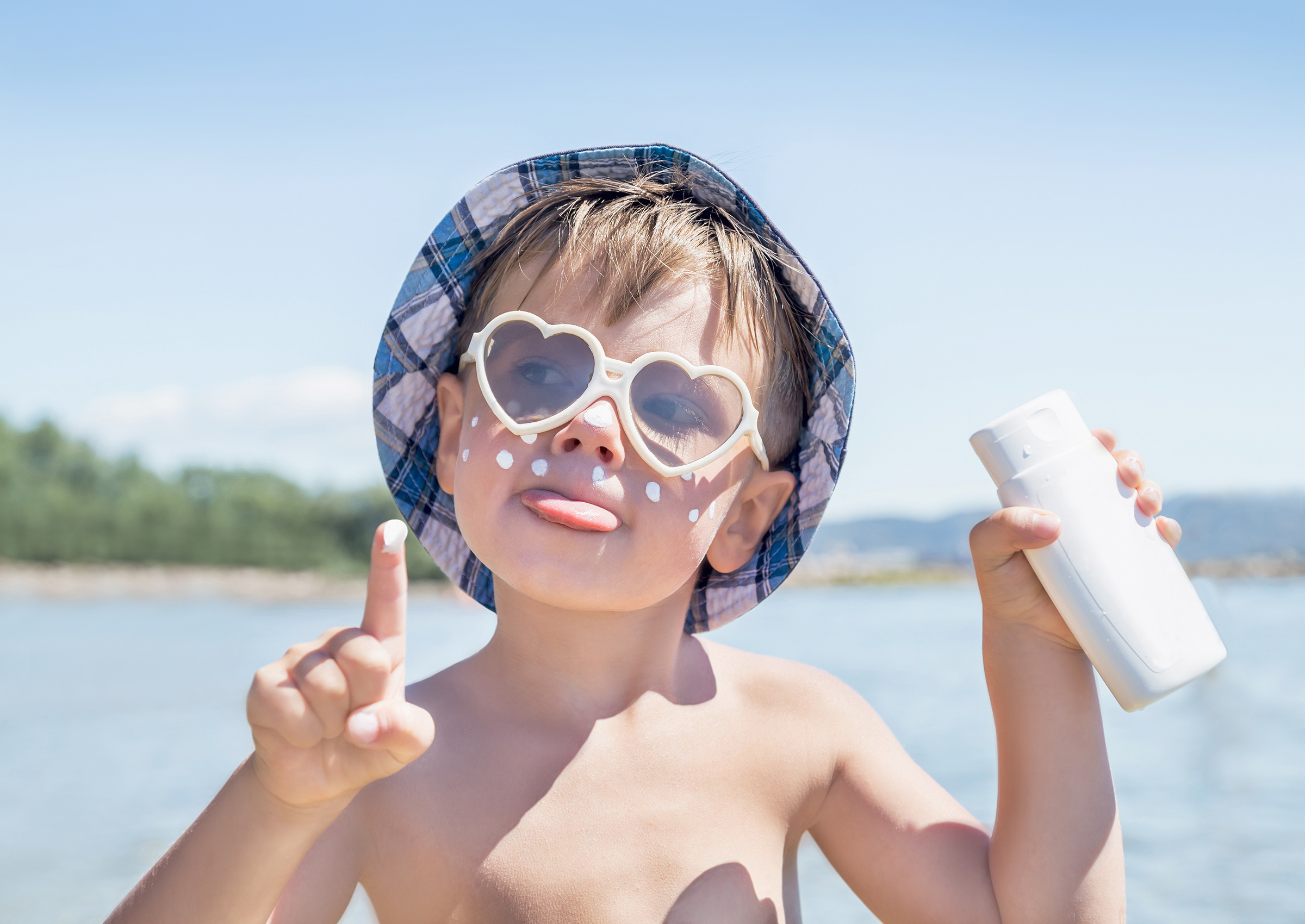 Un enfant portant un chapeau et des lunettes de soleil utilise de la crème solaire.